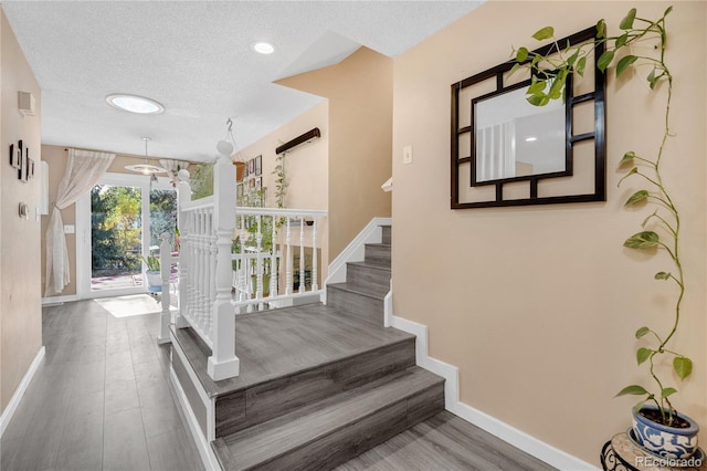 stairs with hardwood / wood-style flooring, a textured ceiling, and a chandelier