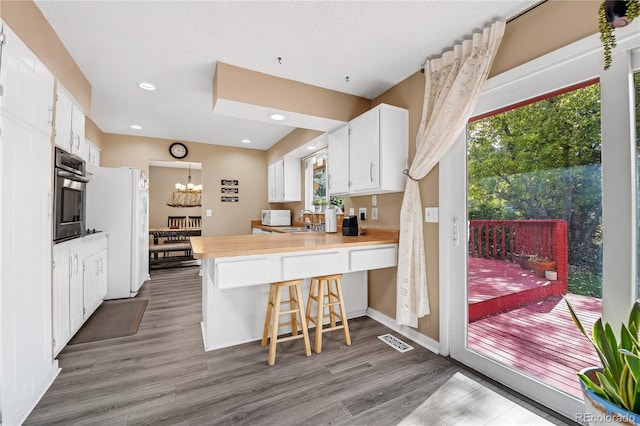 kitchen featuring white appliances, wood-type flooring, kitchen peninsula, white cabinets, and a breakfast bar