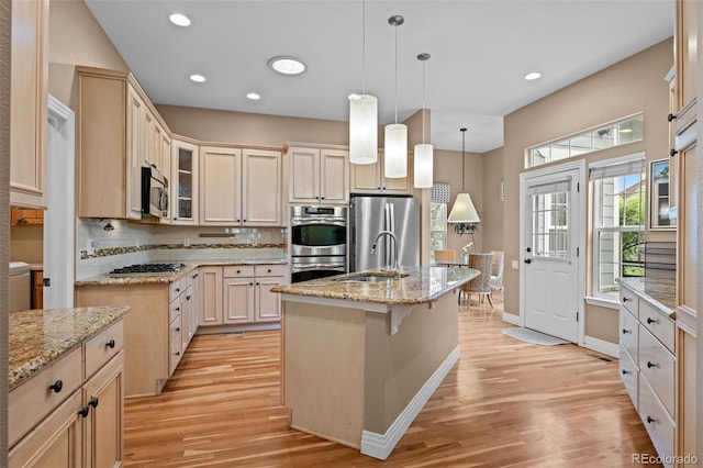 kitchen featuring appliances with stainless steel finishes, light hardwood / wood-style flooring, tasteful backsplash, a center island with sink, and sink