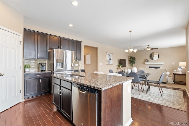 kitchen featuring sink, stainless steel appliances, light stone countertops, a center island with sink, and decorative light fixtures