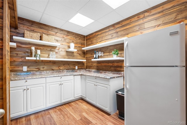 kitchen with white cabinetry, white refrigerator, light hardwood / wood-style floors, light stone countertops, and wood walls