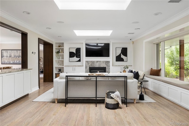 living room featuring built in features, a skylight, crown molding, light hardwood / wood-style floors, and a premium fireplace