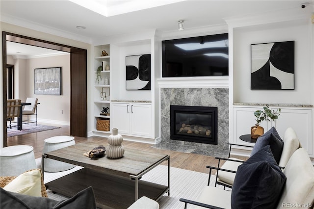 living room with ornamental molding, a high end fireplace, light hardwood / wood-style floors, and built in shelves