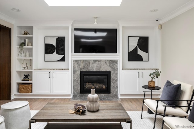 living room with crown molding, light hardwood / wood-style flooring, built in features, and a premium fireplace