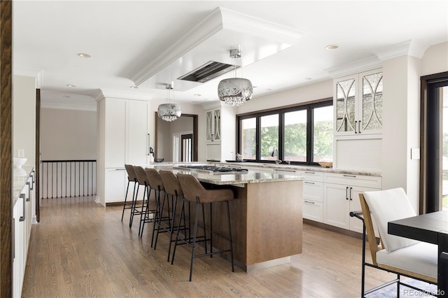 kitchen with pendant lighting, hardwood / wood-style floors, light stone countertops, white cabinets, and a kitchen island