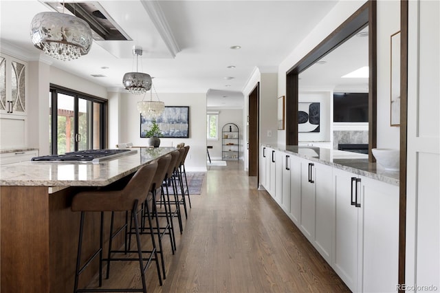 kitchen featuring decorative light fixtures, stainless steel gas stovetop, white cabinets, light stone countertops, and dark wood-type flooring