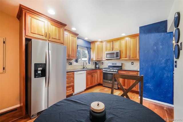 kitchen featuring tasteful backsplash, sink, appliances with stainless steel finishes, and light hardwood / wood-style flooring