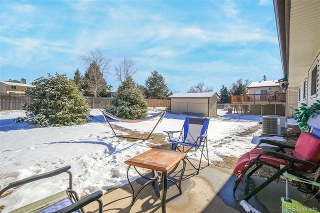 snow covered patio with a deck, central AC unit, and a storage unit