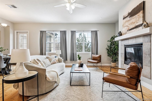 living room with light wood-style flooring, visible vents, a ceiling fan, baseboards, and a tile fireplace