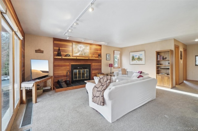 carpeted living area with rail lighting and a glass covered fireplace