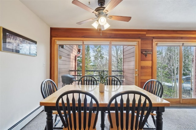 dining area with a baseboard radiator, wooden walls, carpet, and a ceiling fan