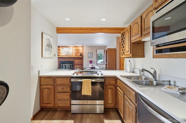 kitchen featuring stainless steel appliances, a sink, wood finished floors, beam ceiling, and light countertops
