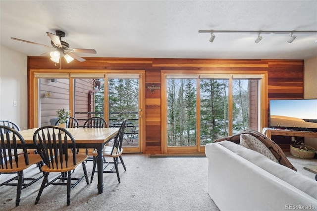 carpeted dining space featuring track lighting, wood walls, and ceiling fan