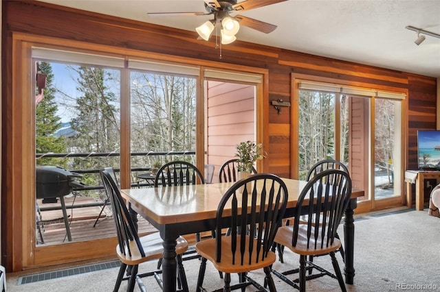dining space featuring a ceiling fan, carpet flooring, track lighting, and wooden walls