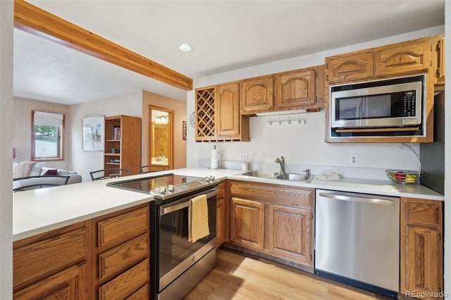 kitchen with appliances with stainless steel finishes, a sink, light countertops, light wood-style flooring, and a peninsula