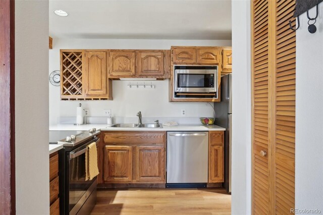 kitchen with stainless steel appliances, a sink, light countertops, light wood-type flooring, and brown cabinetry