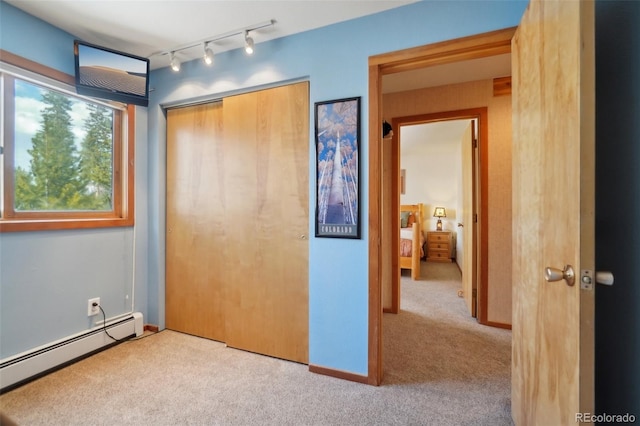 unfurnished bedroom with a baseboard heating unit, carpet, a closet, and rail lighting