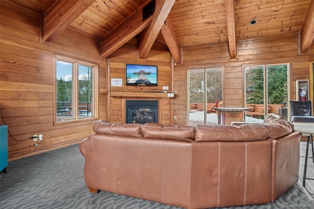 living room featuring beam ceiling, wooden walls, wood ceiling, carpet flooring, and a glass covered fireplace