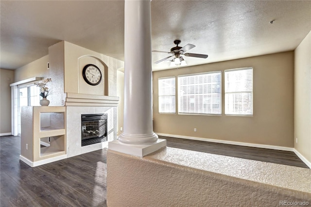 unfurnished living room featuring ornate columns, a textured ceiling, dark hardwood / wood-style flooring, ceiling fan, and a fireplace