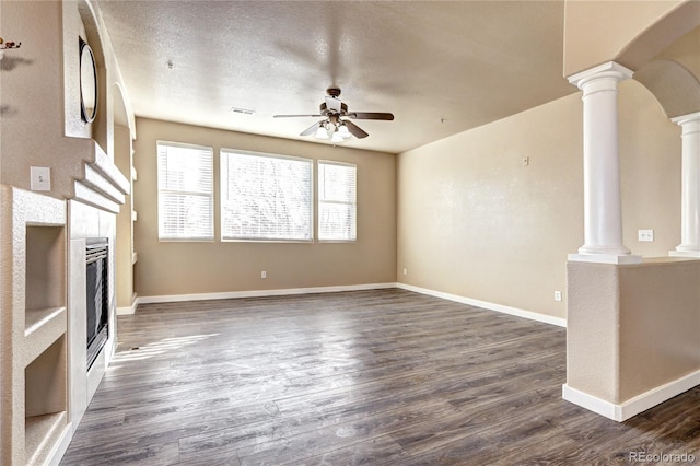 unfurnished living room with ornate columns, a tile fireplace, ceiling fan, dark wood-type flooring, and a textured ceiling