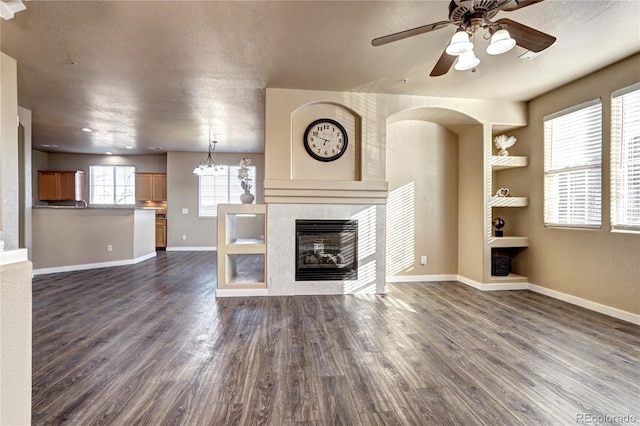 unfurnished living room with a tiled fireplace, ceiling fan with notable chandelier, dark hardwood / wood-style flooring, and a textured ceiling