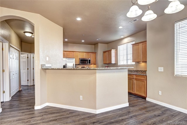 kitchen featuring dark wood-type flooring, hanging light fixtures, stainless steel appliances, light stone counters, and kitchen peninsula