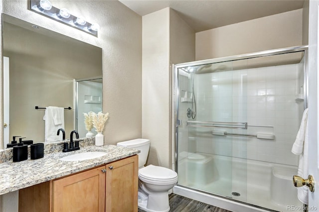 bathroom featuring a shower with door, vanity, hardwood / wood-style flooring, and toilet