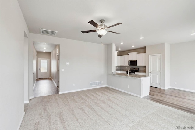 unfurnished living room with ceiling fan, light colored carpet, and sink