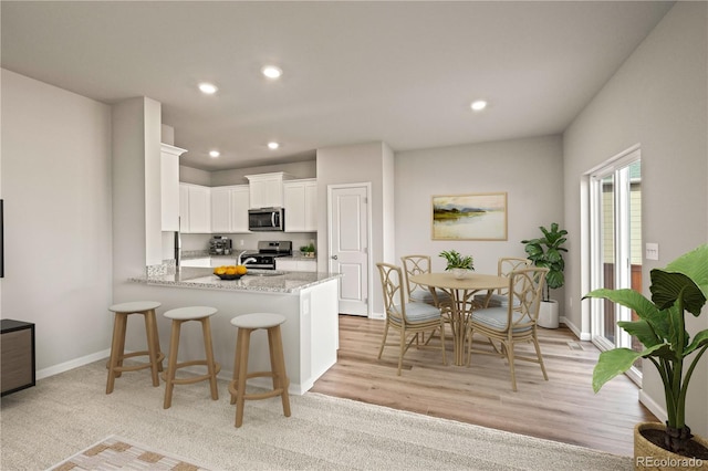 kitchen featuring kitchen peninsula, appliances with stainless steel finishes, light stone countertops, a kitchen breakfast bar, and white cabinets