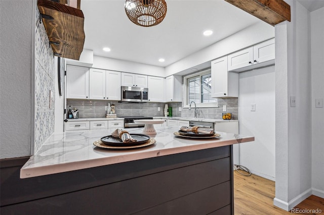 kitchen with stainless steel appliances, white cabinetry, light stone counters, and light hardwood / wood-style flooring