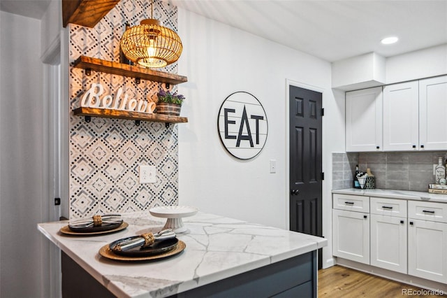 kitchen featuring tasteful backsplash, white cabinetry, light stone countertops, and light hardwood / wood-style floors