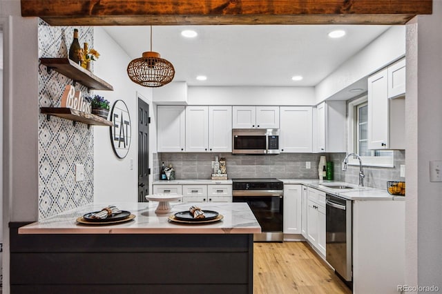 kitchen featuring appliances with stainless steel finishes, decorative light fixtures, white cabinetry, sink, and backsplash