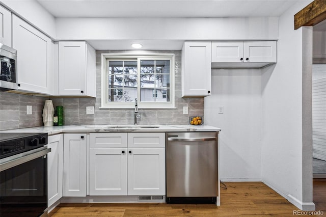 kitchen with sink, hardwood / wood-style flooring, appliances with stainless steel finishes, white cabinets, and decorative backsplash