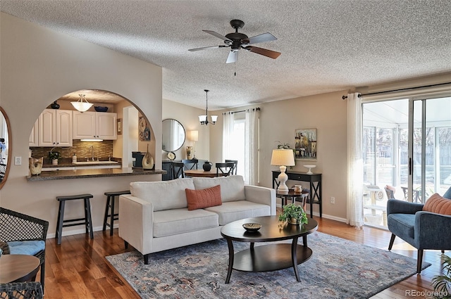 living room featuring ceiling fan with notable chandelier, a textured ceiling, baseboards, and wood finished floors