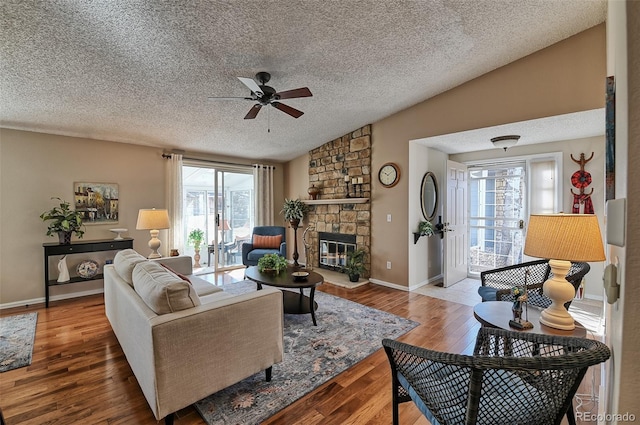 living area featuring lofted ceiling, a textured ceiling, hardwood / wood-style flooring, a fireplace, and a ceiling fan