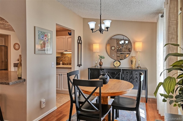 dining room with arched walkways, light wood finished floors, a textured ceiling, a chandelier, and baseboards