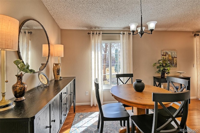 dining area featuring a chandelier, baseboards, a textured ceiling, and light wood finished floors