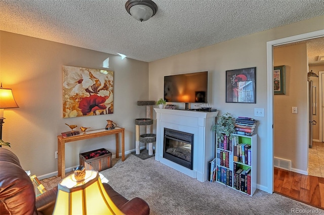 living area featuring a textured ceiling, carpet flooring, visible vents, baseboards, and a glass covered fireplace