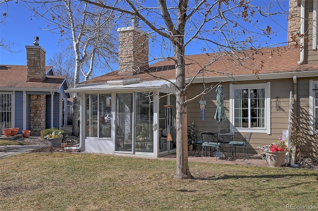 back of property with a sunroom, a shingled roof, a chimney, and a lawn