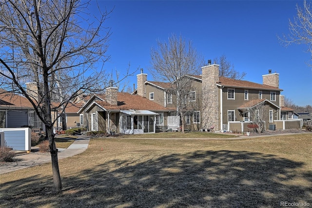 rear view of property with a sunroom, a lawn, and a chimney