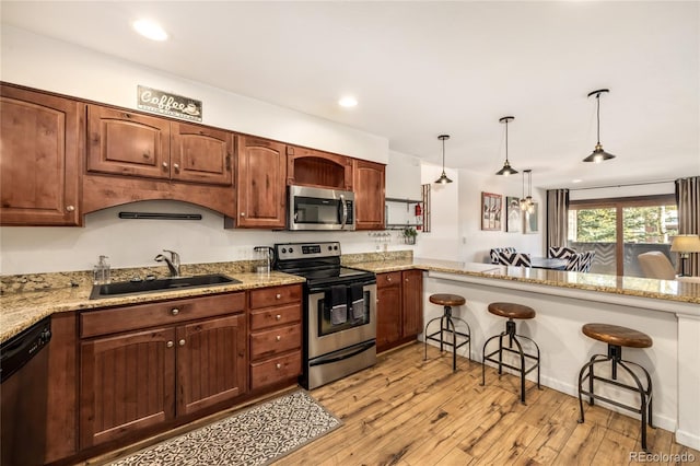 kitchen with light wood-type flooring, a breakfast bar, a sink, stainless steel appliances, and hanging light fixtures