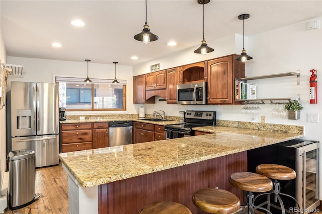 kitchen with light stone countertops, light wood-type flooring, appliances with stainless steel finishes, a peninsula, and a sink