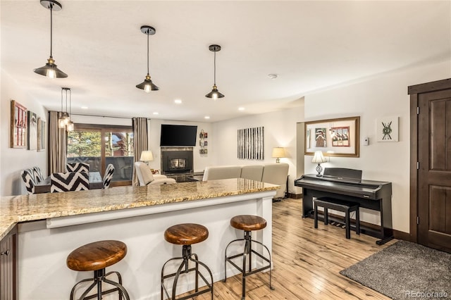 kitchen with a glass covered fireplace, a breakfast bar, light wood-type flooring, and light stone countertops