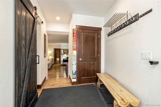 hallway featuring a barn door, light wood-style floors, and baseboards