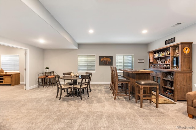 dining room with baseboards, a dry bar, visible vents, and light colored carpet