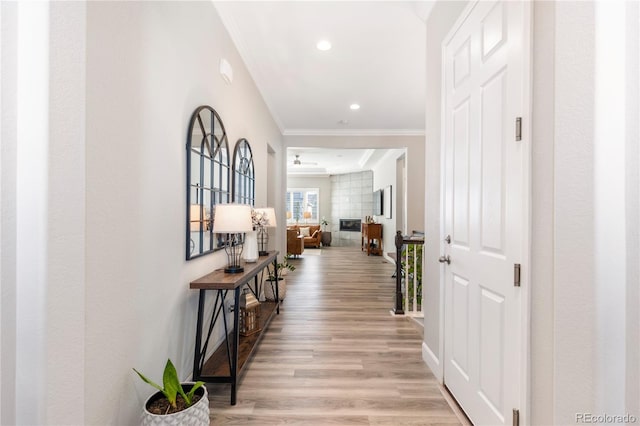 corridor with light wood-type flooring, crown molding, baseboards, and recessed lighting