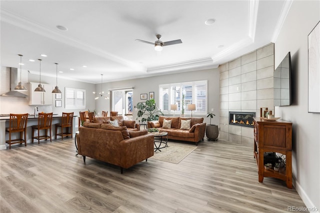 living room with a tile fireplace, crown molding, and light wood-style flooring