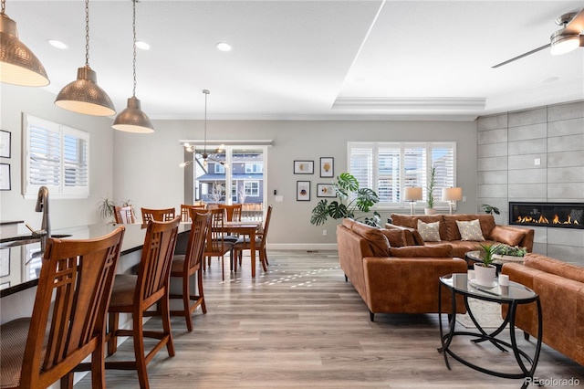 living area with a healthy amount of sunlight, light wood-type flooring, ornamental molding, and a tiled fireplace