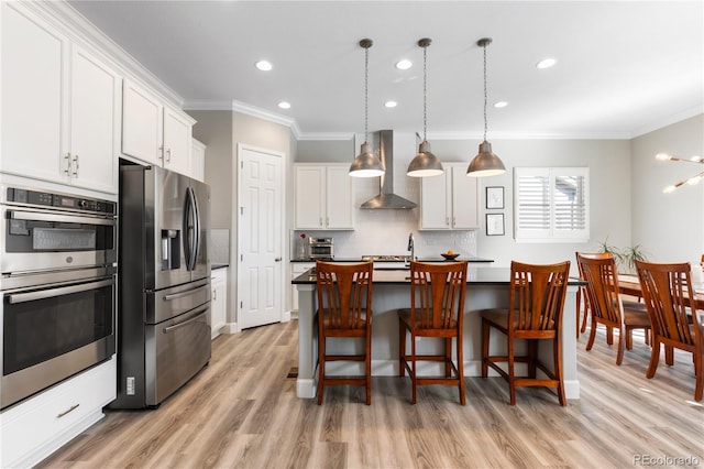 kitchen featuring light wood-style flooring, stainless steel appliances, white cabinets, decorative backsplash, and wall chimney exhaust hood