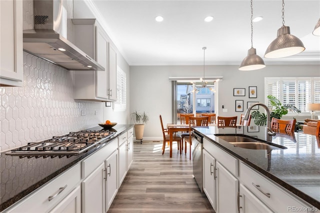 kitchen featuring a sink, wall chimney range hood, appliances with stainless steel finishes, decorative backsplash, and crown molding